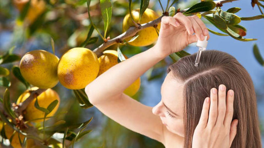 donna che applica l'olio di argan sui capelli con una pianta di argan sullo sfondo